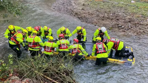 Mid and West Wales Fire and Rescue Service Fourteen people all wearing high-vis jackets are seen with an inflatable sled on a river, transporting Nicky the donkey