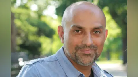 Essex Cultural Diversity Project A man wearing a blue shirt and is smiling at the camera