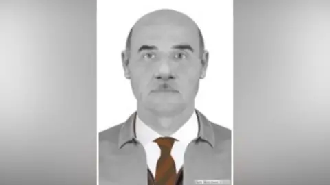A police image of a man with no hair at the top of his head, with a red tie and a grey anorak and a white shirt.