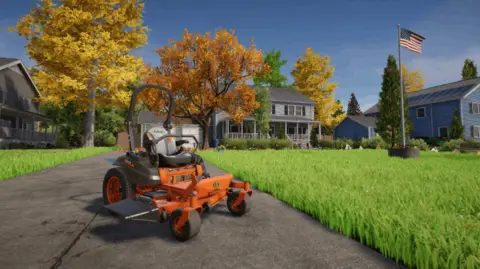 Skyhook Games An in-game screenshot from the game Lawn Mowing Simulator 2. It shows an organe American lawn mower on a pathway next to a lawn of green grass. The American flag flies from a straight grey pole on the lawn and behind it is a grey house, surrounded by trees with orange and yellow leaves.