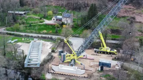 A large yellow crane to the right of a bridge