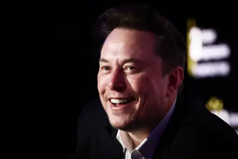 Getty Images Elon Musk smiling in black suit with white shirt