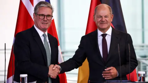 Reuters Prime Minister Sir Keir Starmer shakes hands with German Chancellor Olaf Scholz in front of UK and German flags at a news conference in Berlin