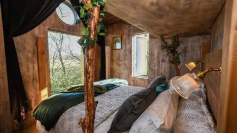 Faraway Treehouses A wooden bedroom inside a treehouse holiday home. Paisley bedding and green cushions, throws and curtains are used as decoration for the room. 