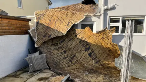 The underside of a roof laying over the garage and onto the floor of a patio. 