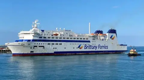 BBC A white ferry with blue tipped chimneys with the words Brittany Ferries on the side arriving in St Peter Port Harbour.