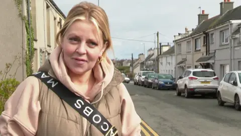 Woman wearing light-coloured coat standing in front of a street of houses