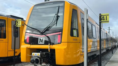 Close up of a new yellow, grey and black Metro train. There is a post with the sign saying 41 to the right of it. The skies are grey. 