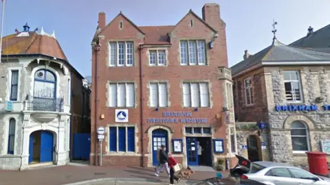 A picture of the outside of the museum. It is a brick building with the name of the museum in blue on the front of it. 