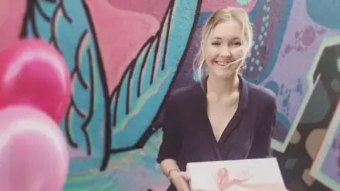 Toyah Cordingley holding a box and standing in front of a colourful wall