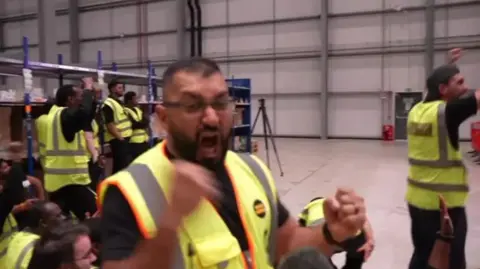 Workers in a distrubution warehouse celebrate the win.