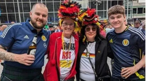 Martina Spiech Martina Spiech, in a Germany football jersey, a red jacket and a hat in the Germany colours of red, yellow and black, poses with a similarly dressed friend, and two Scotland fans in their Scotland tops in the town square ahead of the Cologne game.