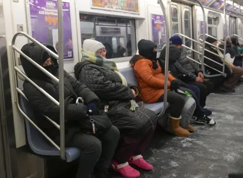 People sit bundled up with hats, scarfs and boots on a New York train