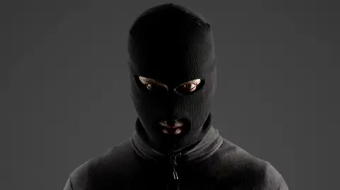 Getty A person wearing a black balaclava and a black jumper, looking directly at the camera. 