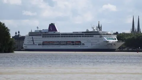 A large cruise ship, which is white, with purple and green markings, is seen docked at a port 