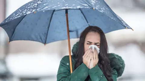 A generic image of a woman with an umbrella sneezing into a tissue