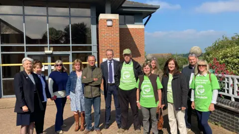 Group of people, some wearing green Staunch campaign T-shirts, stand outside the council offices in Thrapston.