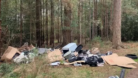 Forestry England Cardboard, bin bags and white goods litter a forest clearing.