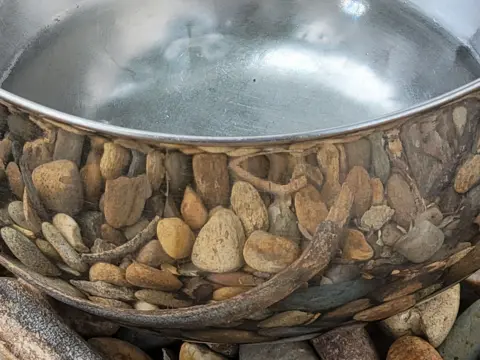 Linda Alkove Rockes reflected in the outside of a metal saucepan