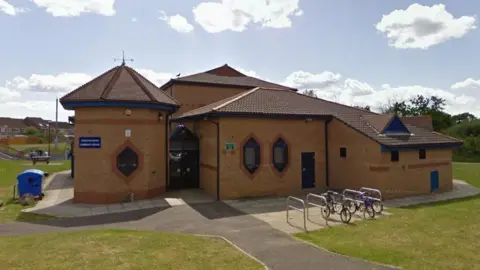 Google A more modern-looking building with red bricks and hexagonal windows set in a green space.