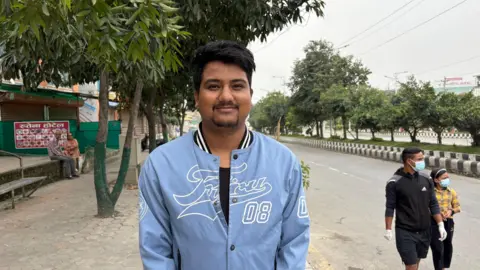 A man standing in a blue jacket in front of the street 