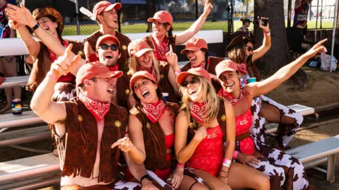 Kaktus Scot A group of people dressed as cowboys sitting on tiered benches, many with their hands up in the air and cheering
