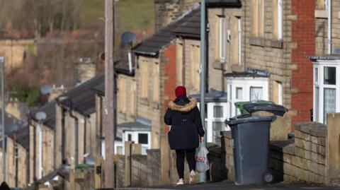 Woman walking in front of a row of houses in Huddersfield