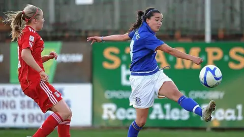 Getty Images Two female football players, one with long brown hair and the other with long blonde hair, playing the sport on the pitch