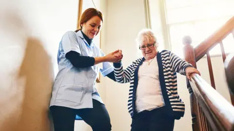 Getty Images Carer membantu wanita yang lebih tua menuruni tangga - mereka berdua tersenyum