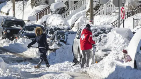 Getty Images Residents shovel snow on a street in a neighbourhood of Boston, Massachusetts, a day after the region was hit with a "bomb cyclone", 5 January 2018
