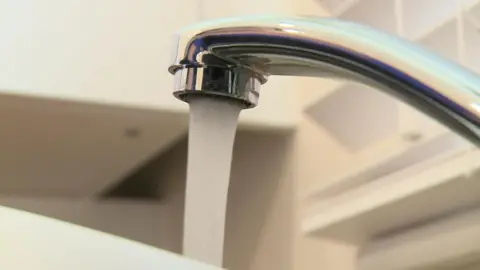 Close-up of a silver water tap with water flowing out of it