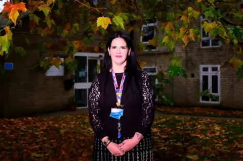 BBC Cristin Casey with brown hair poses under a tree and in front of a brick building