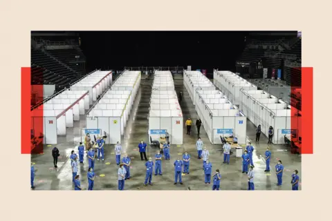 Getty Images Vaccinators in blue uniforms are infront of rows of vaccine booths