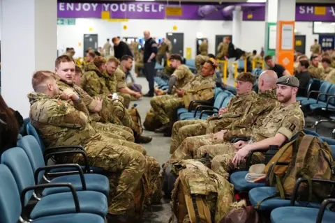PA Media/Owen Humphreys Soldiers sit opposite each other in the waiting lounge. They have bags and are wearing their army camouflage uniforms.