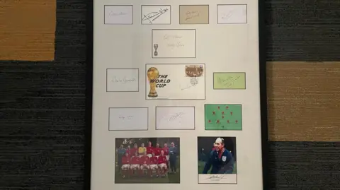 NICK WILSON/BBC The piece appears to be a collectible tribute to football history, most likely linked to the FIFA World Cup and notable players or teams. The combination of autographs, a team photo, and the World Cup trophy imagery suggests it is a commemorative display celebrating a significant era or achievement in football.