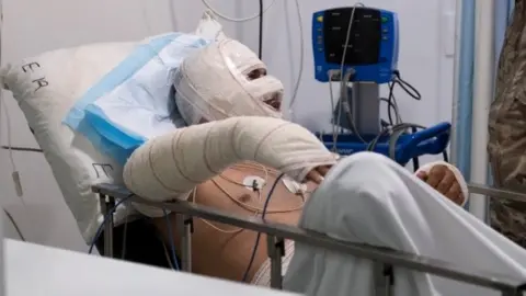 A Lebanese soldier speaks to a man injured in a petrol tank explosion in Akkar at a hospital in Beirut (15 August 2021)