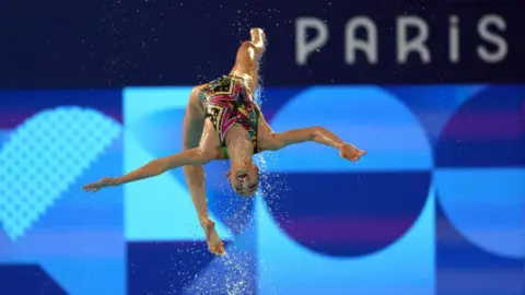 Amin Mohammad Jamali / Getty Images A member of the Egyptian synchronized swimming team performs a daring somersault during the Paris Olympic Games in France - Wednesday, August 7, 2024 