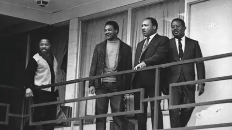 AP photo/Charles Kelly A black and white film photo of Martin Luther King Jr (second R) stands with Hosea Williams (L), Jesse Jackson (second L), and Ralph Abernathy (R) on the balcony of a Memphis hotel on 3 April 1968, taken the day before King was assassinated.