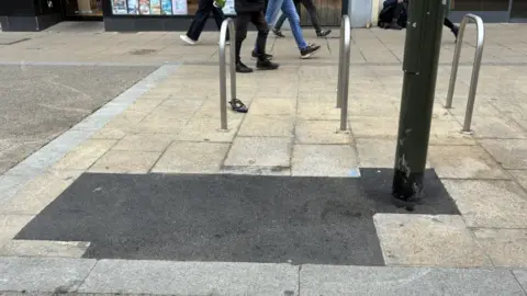 Tarmac replacing stone slabs on the pavement. It looks out of place compared to the original stones. 