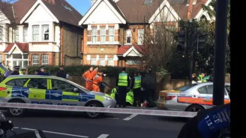 The scene of the crash. A road with police tape, emergency service workers and police cars