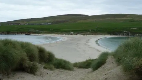 a beach which has water on either side and hills in the background