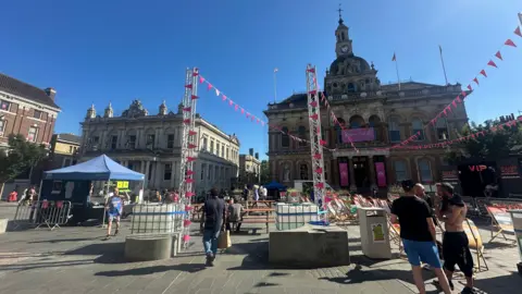 Alice Cunningham/BBC Ipswich Cornhill where pink bunting has been put up leading to the Town Hall. People walk nearby and sit on beach style deck chairs. 