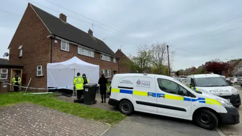 Stephen Huntley/BBC Police in Rothmans Avenue, Great Baddow. There are several police vans, a cordon and a forensic tent that has been put up. There are police officers standing at the property.