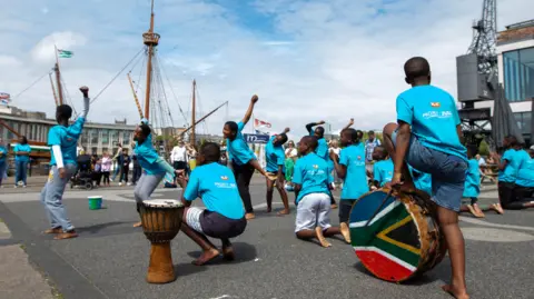 The South African choir performing outside the M-shed in Bristol. Some have south african painted drums and are dancing.