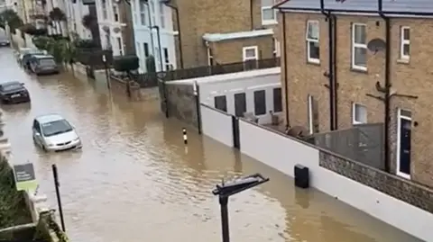 Dan Thomas A photo from an upstairs window shows a fully-submerged street in Ryde, with brown water halfway up the wheels of cars.