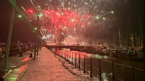 Whitehaven Town Council Fireworks over Whitehaven Harbour with boats to one side. The sky is red and gold and white.