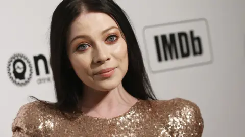 Getty Images Michelle Trachtenberg appears at a red carpet event wearing a gold sequin dress.