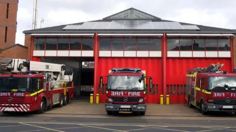 Stock image of three fire engines parked outside a fire station in the UK