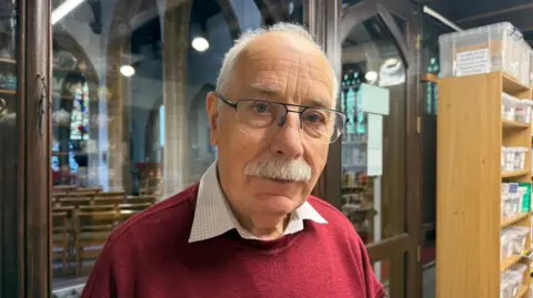 Man in red jumper with glasses and moustache looks at the camera.