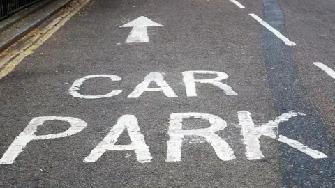 Getty Images A road where the words car park has been painted on in white paint. There is a white arrow above the words directing drivers to the car park.